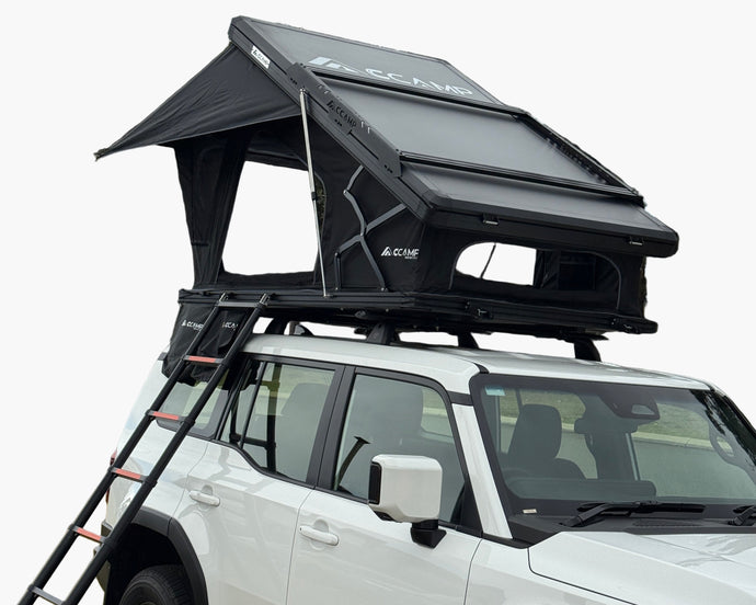 White SUV with a rooftop tent and ladder on a grassy area with trees in the background
