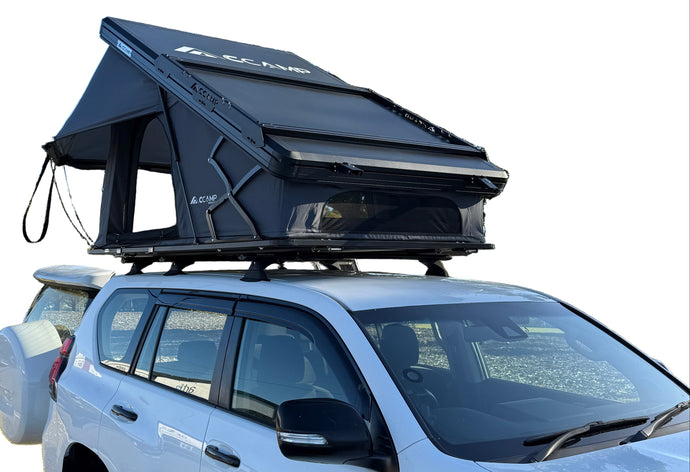White car with a camper shell parked on a road with trees in the background