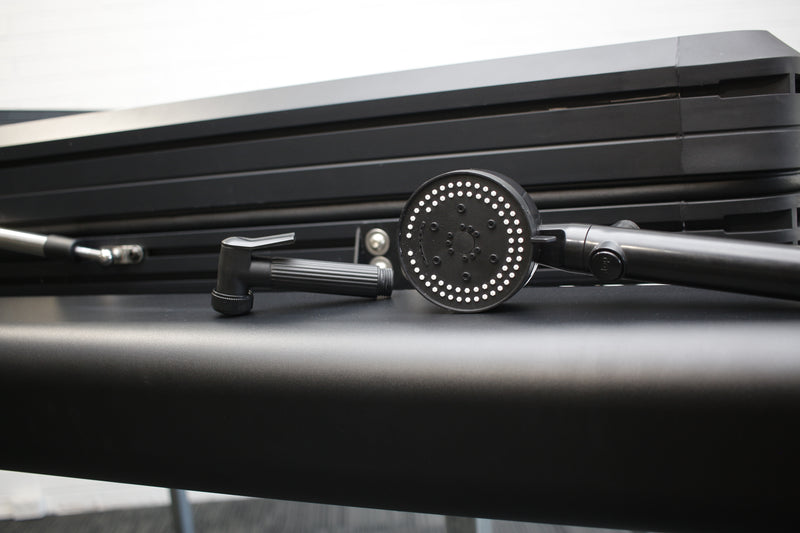 Load image into Gallery viewer, Close-up of a black shower head and hose on a metallic surface with a blurred background
