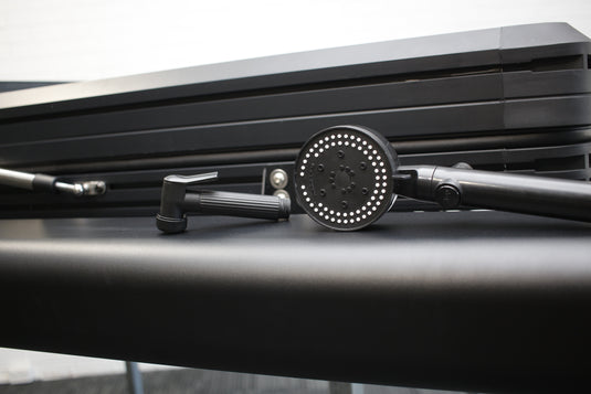 Close-up of a black shower head and hose on a metallic surface with a blurred background