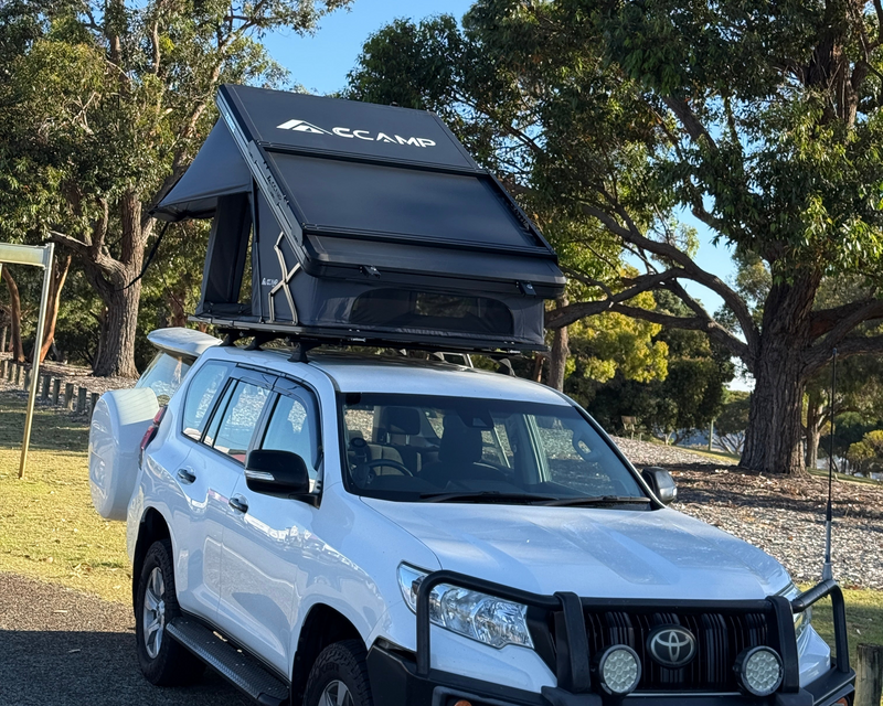 Load image into Gallery viewer, White SUV with a rooftop tent parked in a natural setting with trees.
