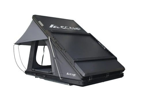 Black CCamp roof tent on display against a white brick wall.